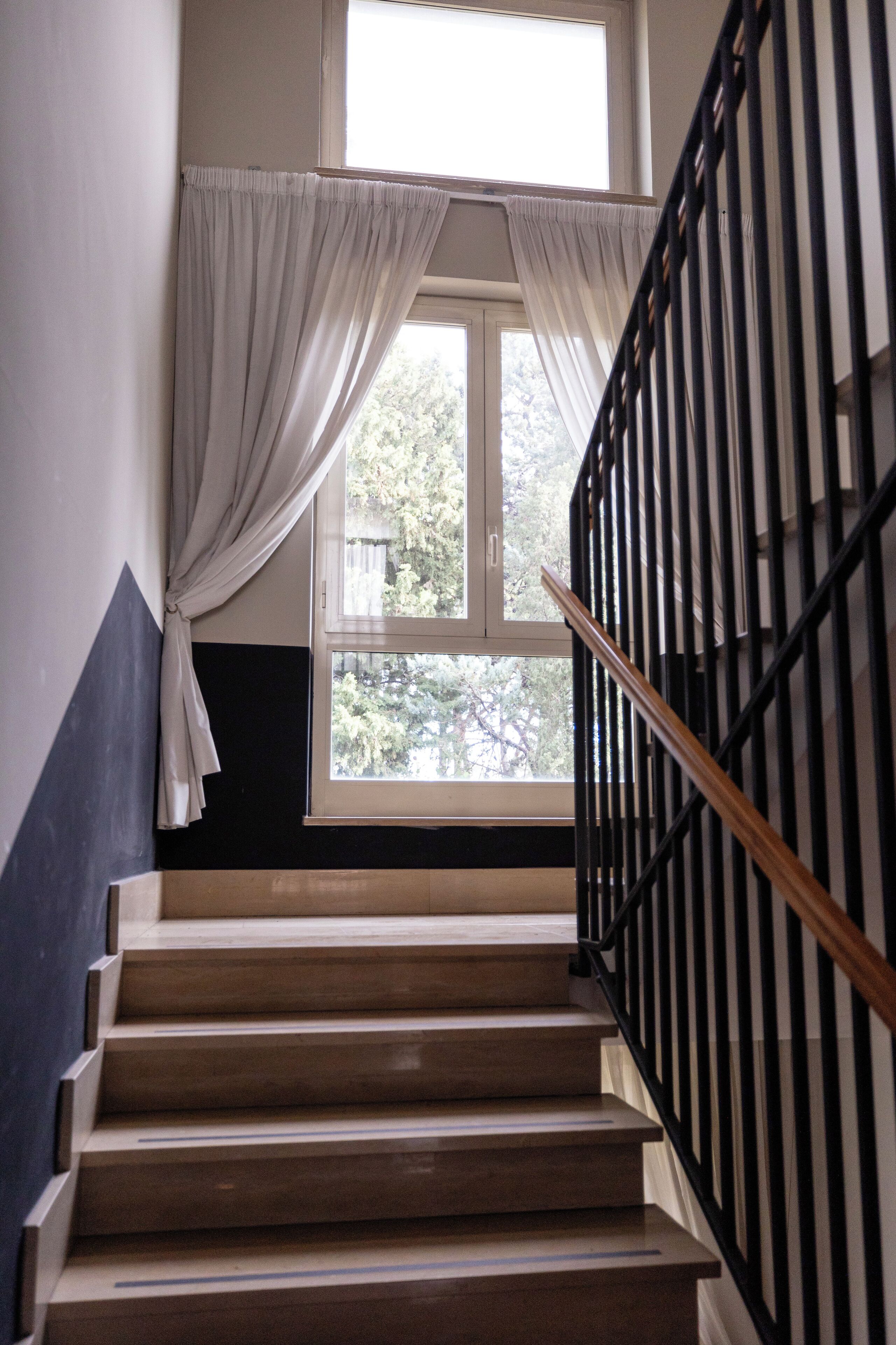 A staircase with a black railing and a window with white curtains.