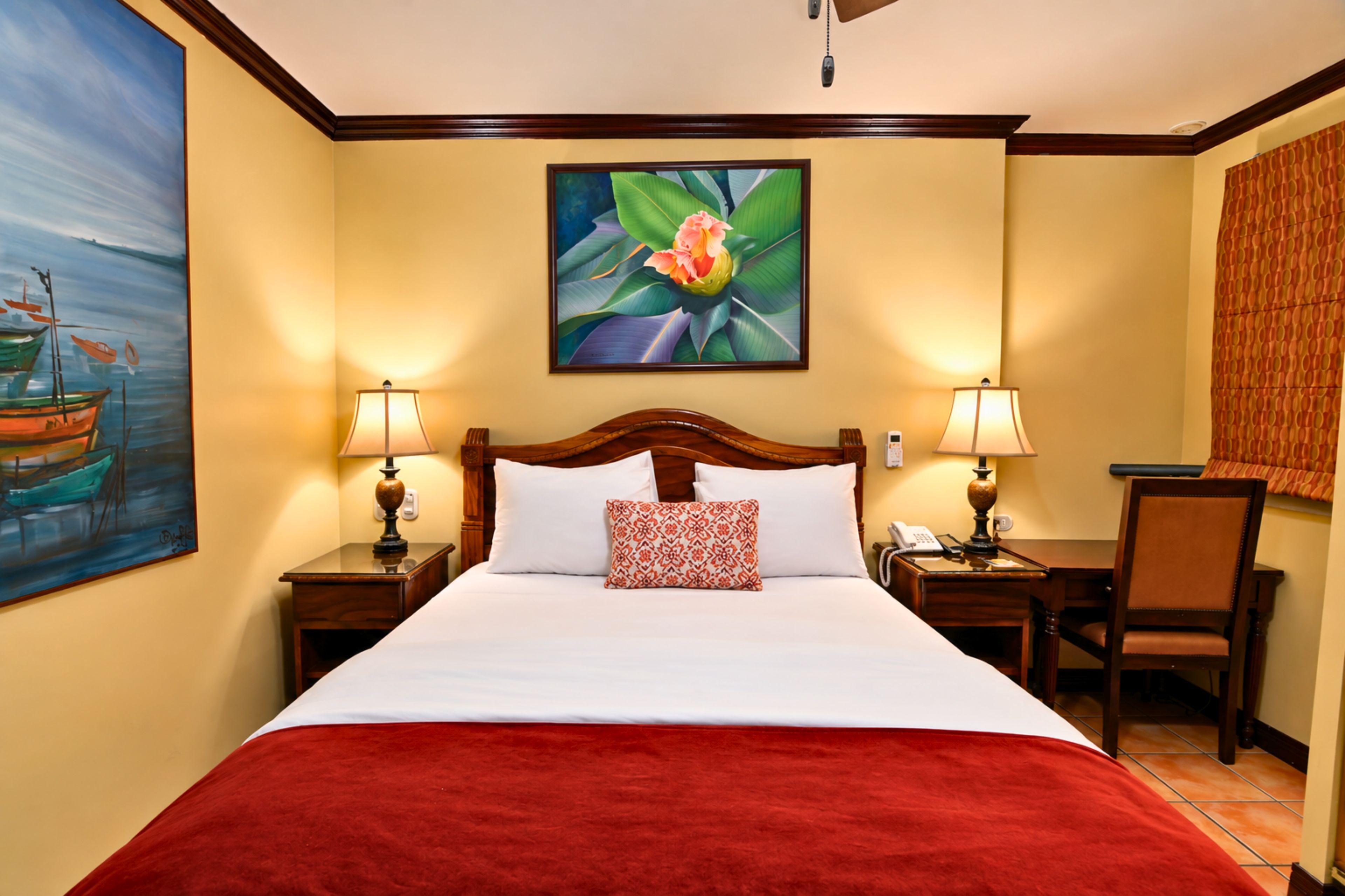 Quarto de hotel com uma cama grande, duas luminárias de cabeceira, um quadro na parede e uma cadeira.