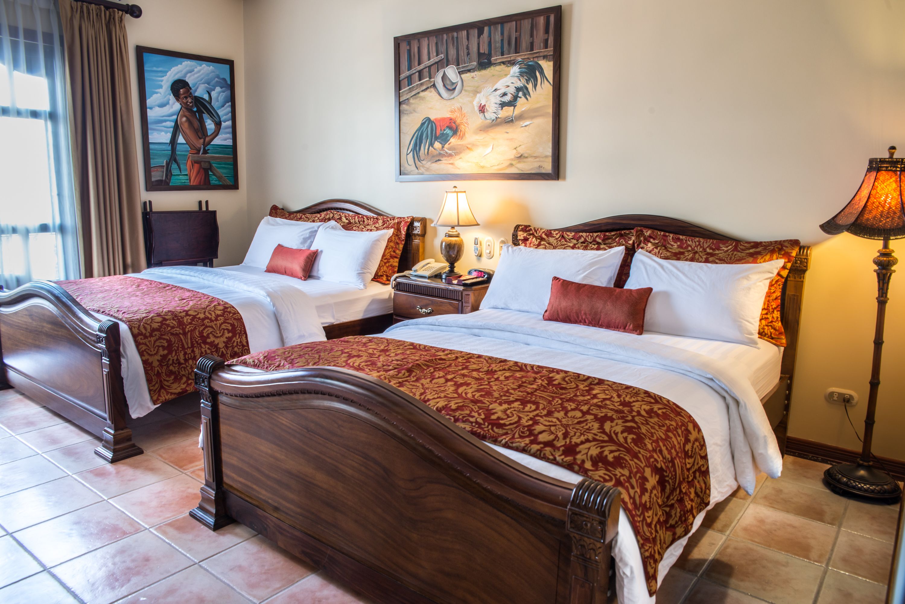 Habitación doble con dos camas, una mesita de noche, una lámpara y cuadros en las paredes.