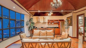 A spacious living area with a wooden ceiling, a large sofa, a dining table, and a kitchen in the background. - Hotel Casa Roland San José (San José)