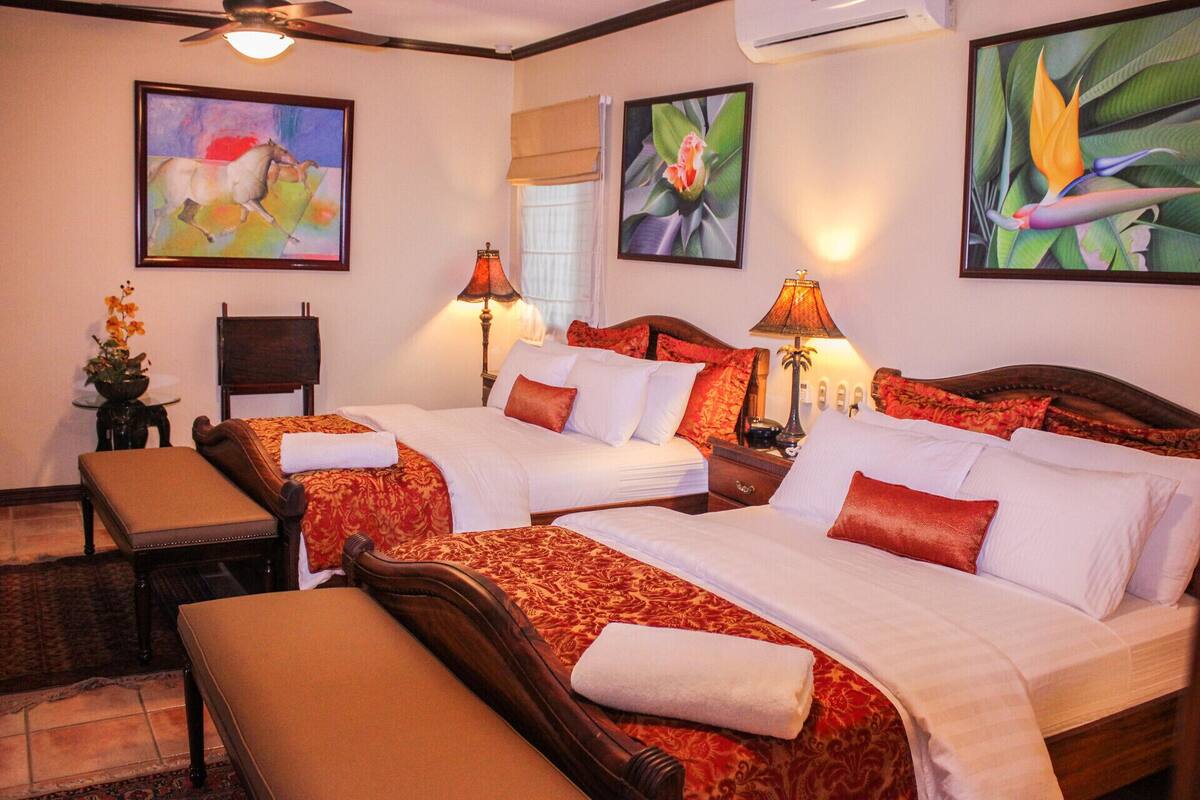 A hotel room with two beds, a bench, a chair, and artwork on the walls.