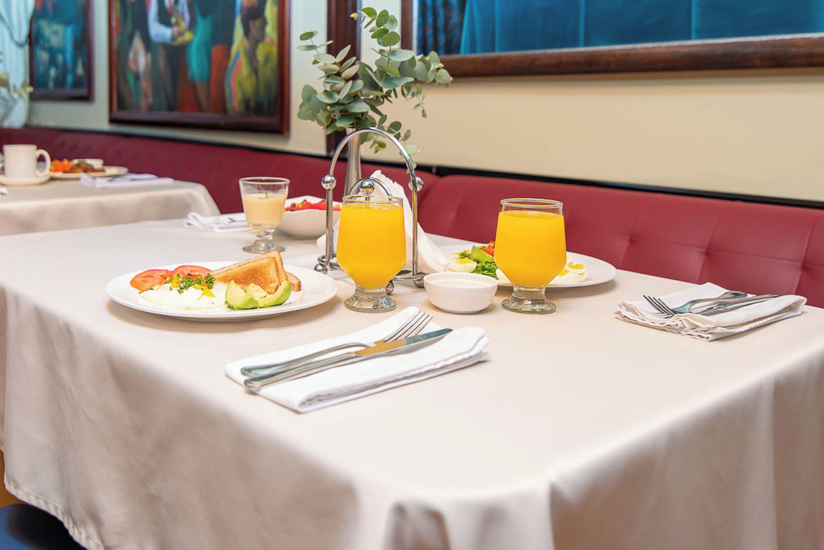 A breakfast table set with plates of food, glasses of orange juice, and a vase with a plant.