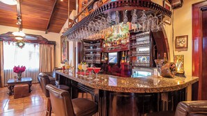 A bar area with a granite countertop, multiple bar stools, and a variety of bottles and glasses. - Hotel Casa Roland San José (San José)