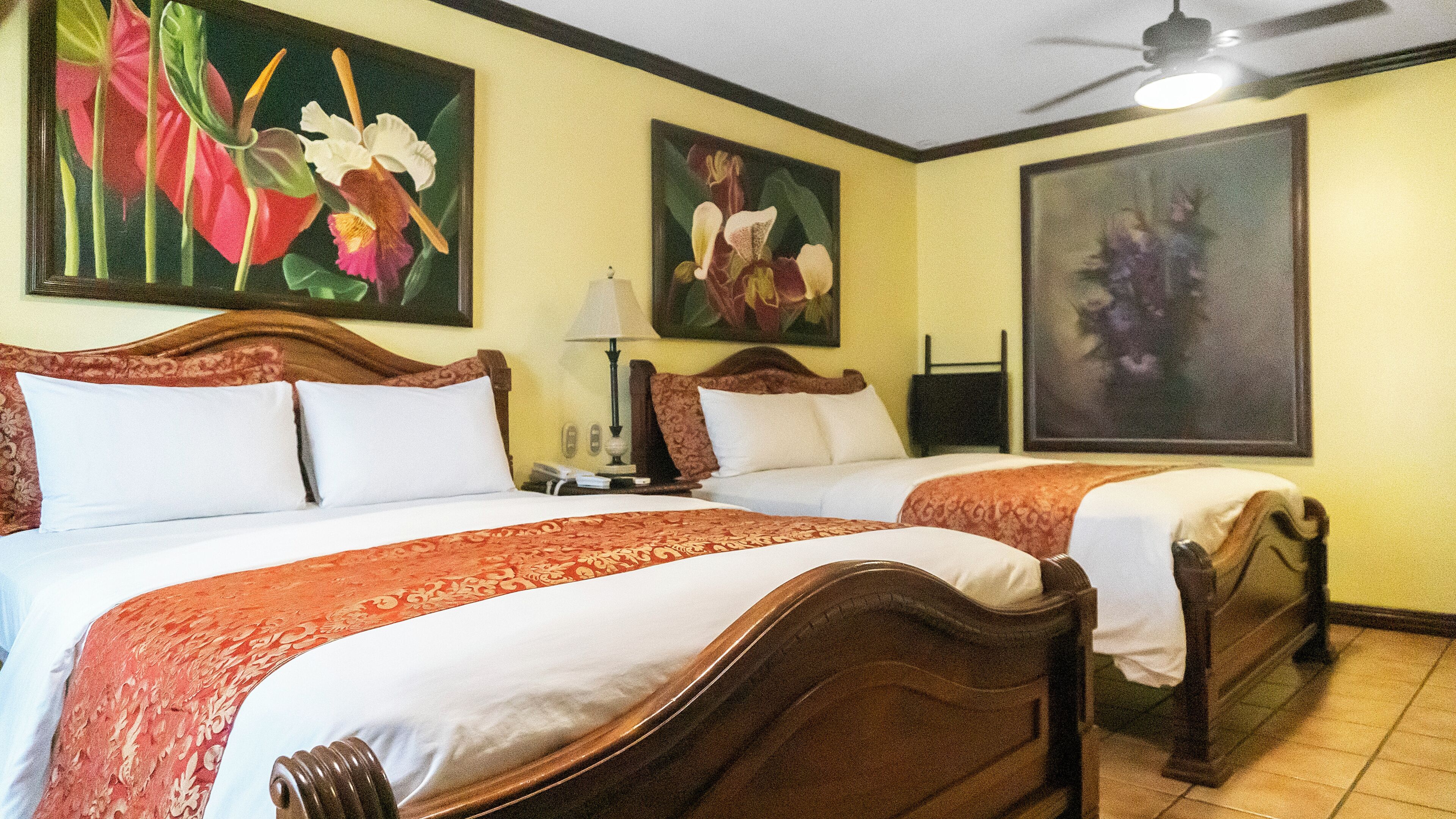 Habitación de hotel con dos camas, ventilador de techo y obras de arte en las paredes.