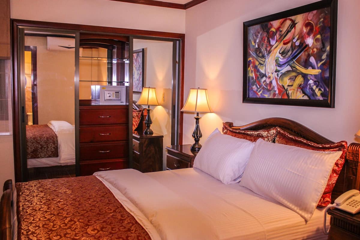 A hotel room with a bed, a dresser, a mirror, a painting, and a telephone.