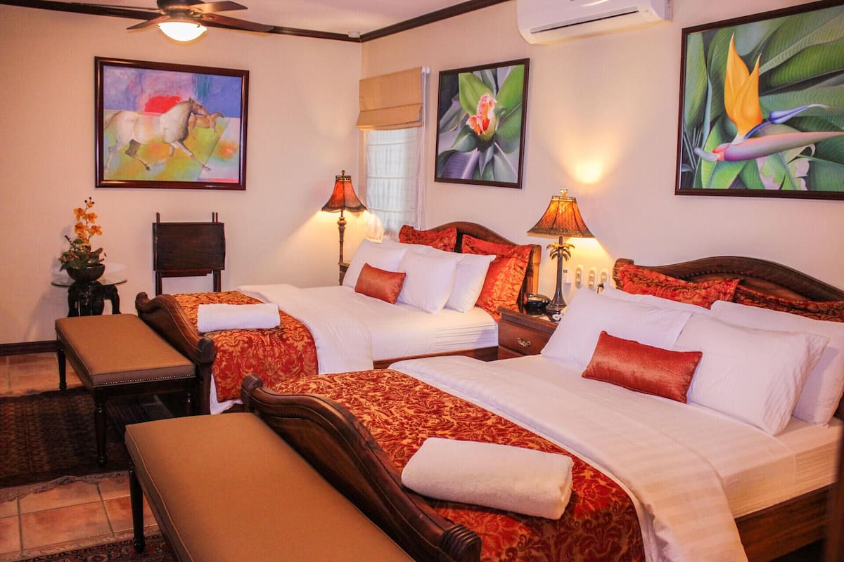 A hotel room with two beds, a bench, a chair, and artwork on the walls.