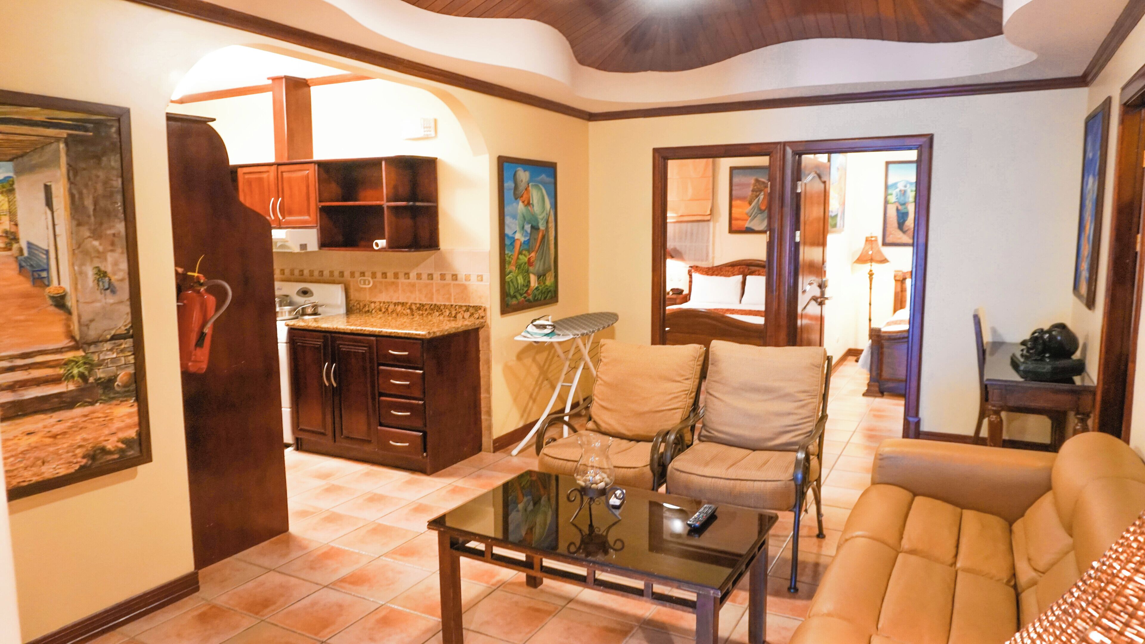 Una sala de estar con sofá, una mesa de centro de vidrio y una zona de cocina con armarios y estufa.