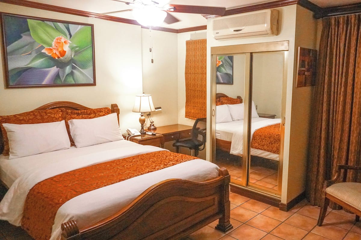 A hotel room with a bed, bedside table, lamp, chair, and a mirror.