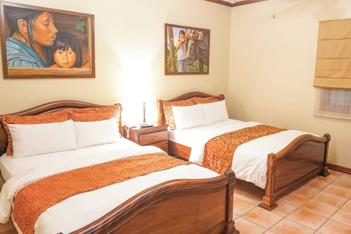 A hotel room with two wooden beds, a nightstand, a chair, and two paintings on the wall.