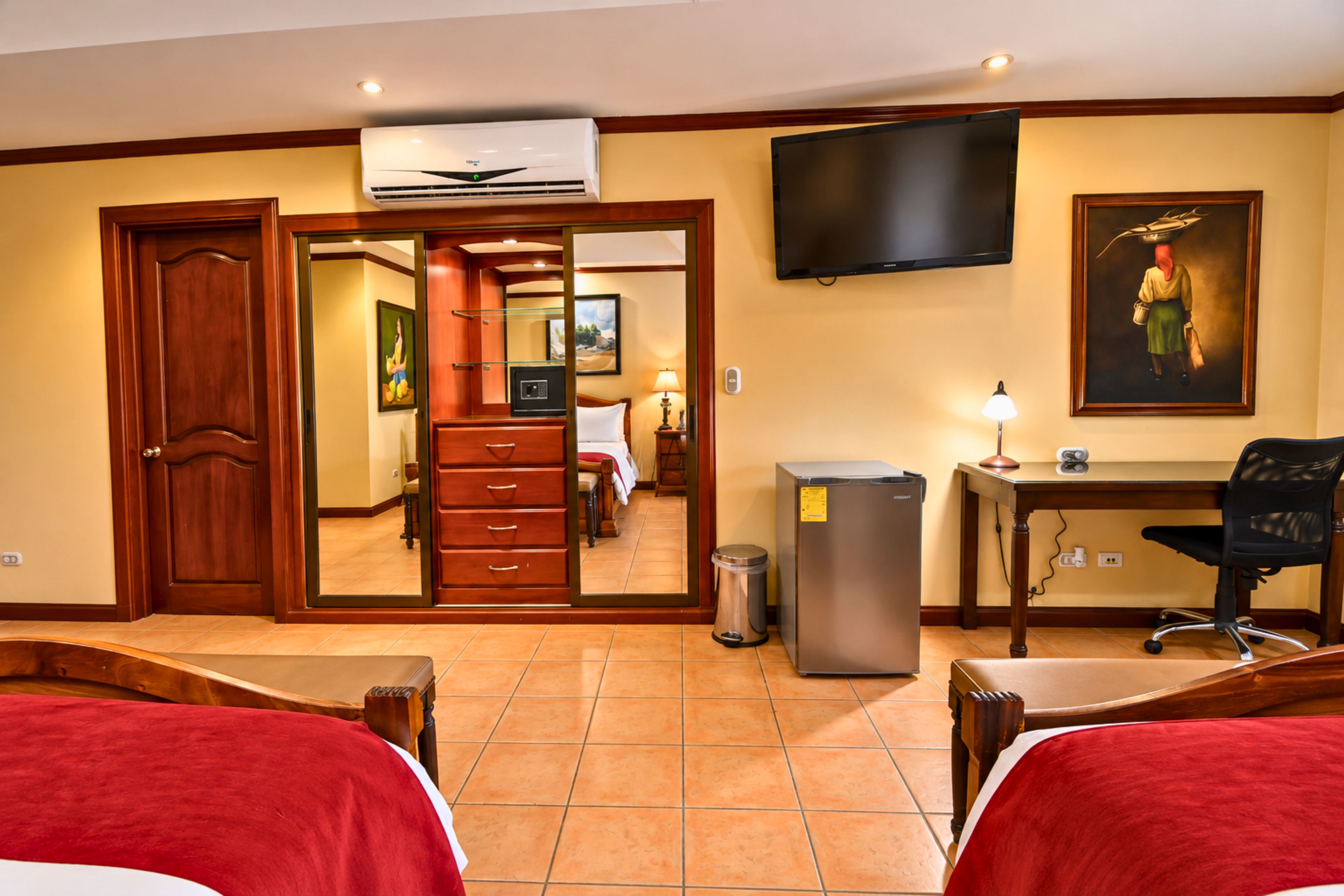 A hotel room with a bed, a desk, a chair, a television, and a trash can.