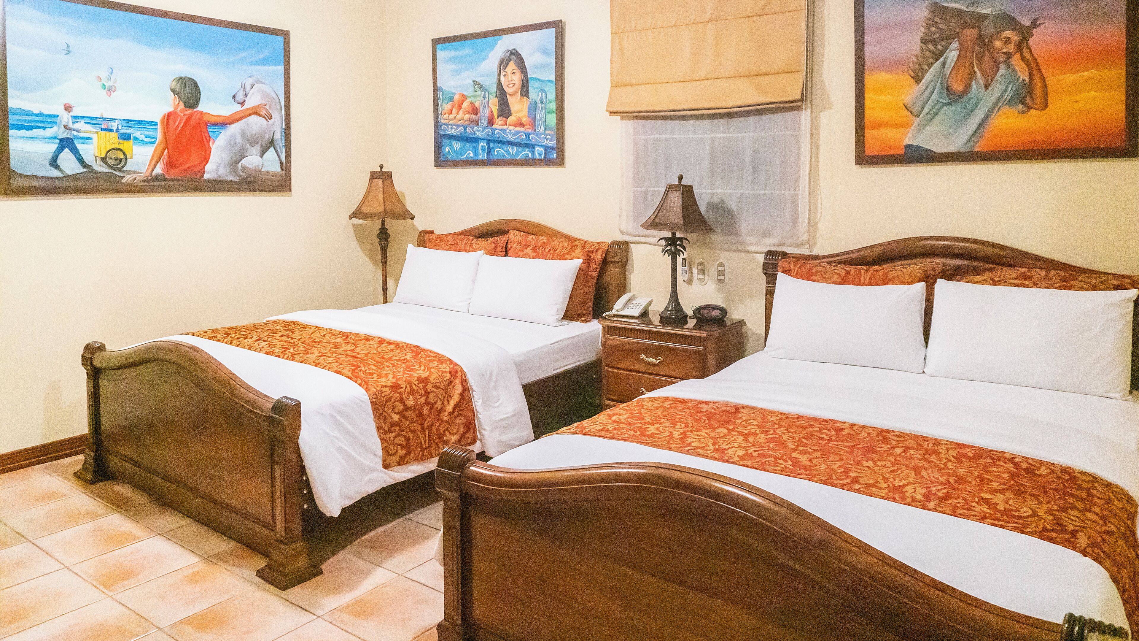 A hotel room with two wooden beds, a nightstand, a lamp, and wall art.