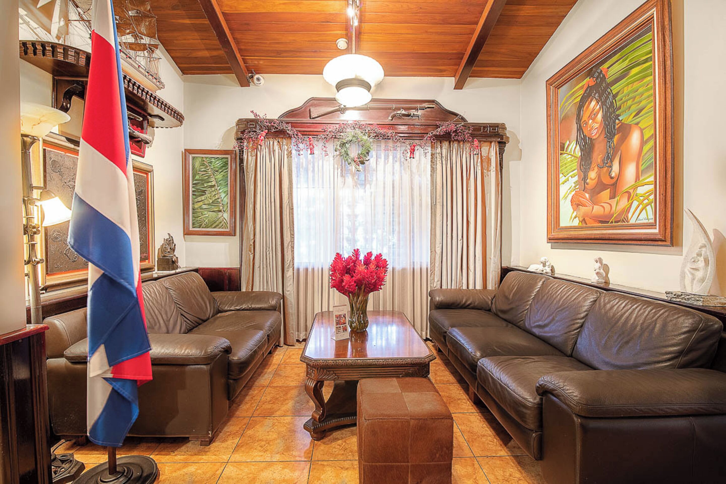 A living room with two leather sofas, a wooden coffee table with a vase of flowers, a flag, and a painting on the wall.