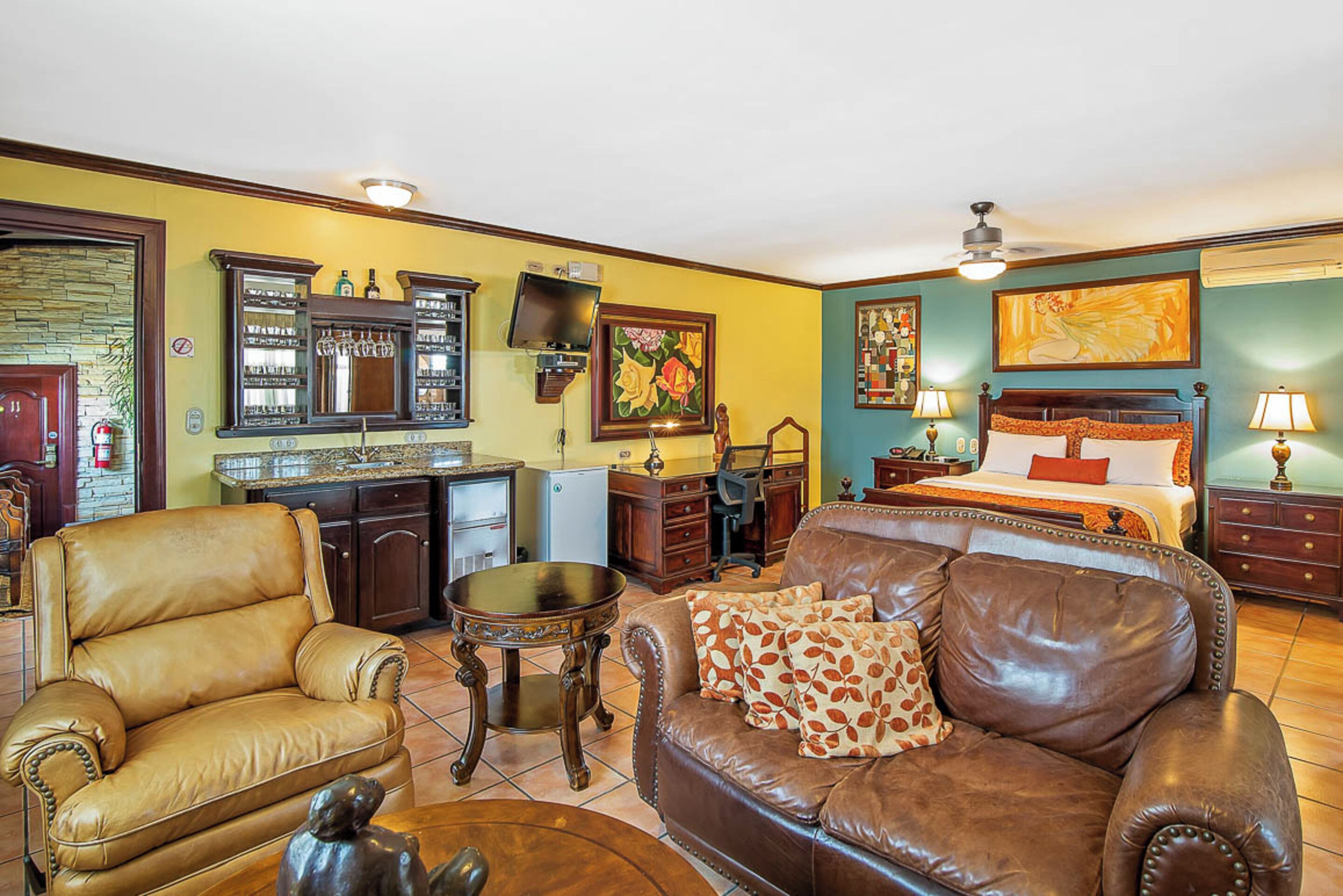 A hotel room with a bed, a sofa, a chair, a desk, and a kitchen area.