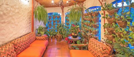 A room with a wooden ceiling, a chandelier, orange sofas, and hanging plants.