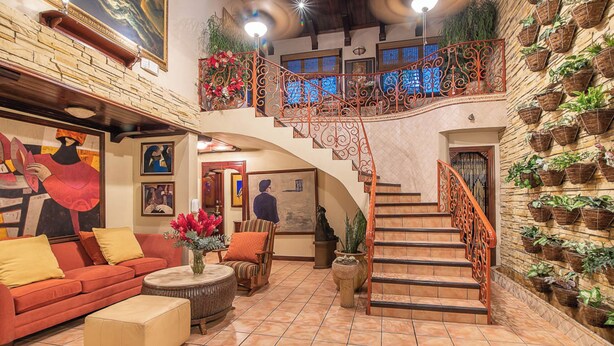 A spacious living area with a red sofa, a coffee table, and a staircase with a wrought iron railing. - Hotel Casa Roland San José (San José)