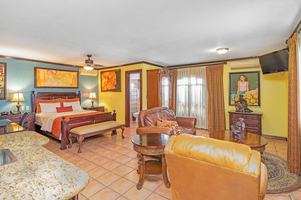 A hotel room with a bed, a sofa, a dining table, and a TV.