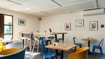 A modern dining area with multiple tables and chairs, framed artwork on the walls, and a window providing natural light.