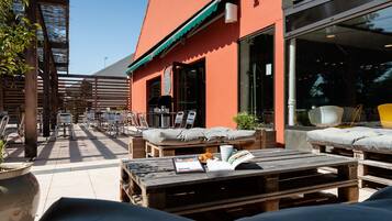 An outdoor seating area with wooden tables and chairs, a wooden fence, and a building with a red facade.