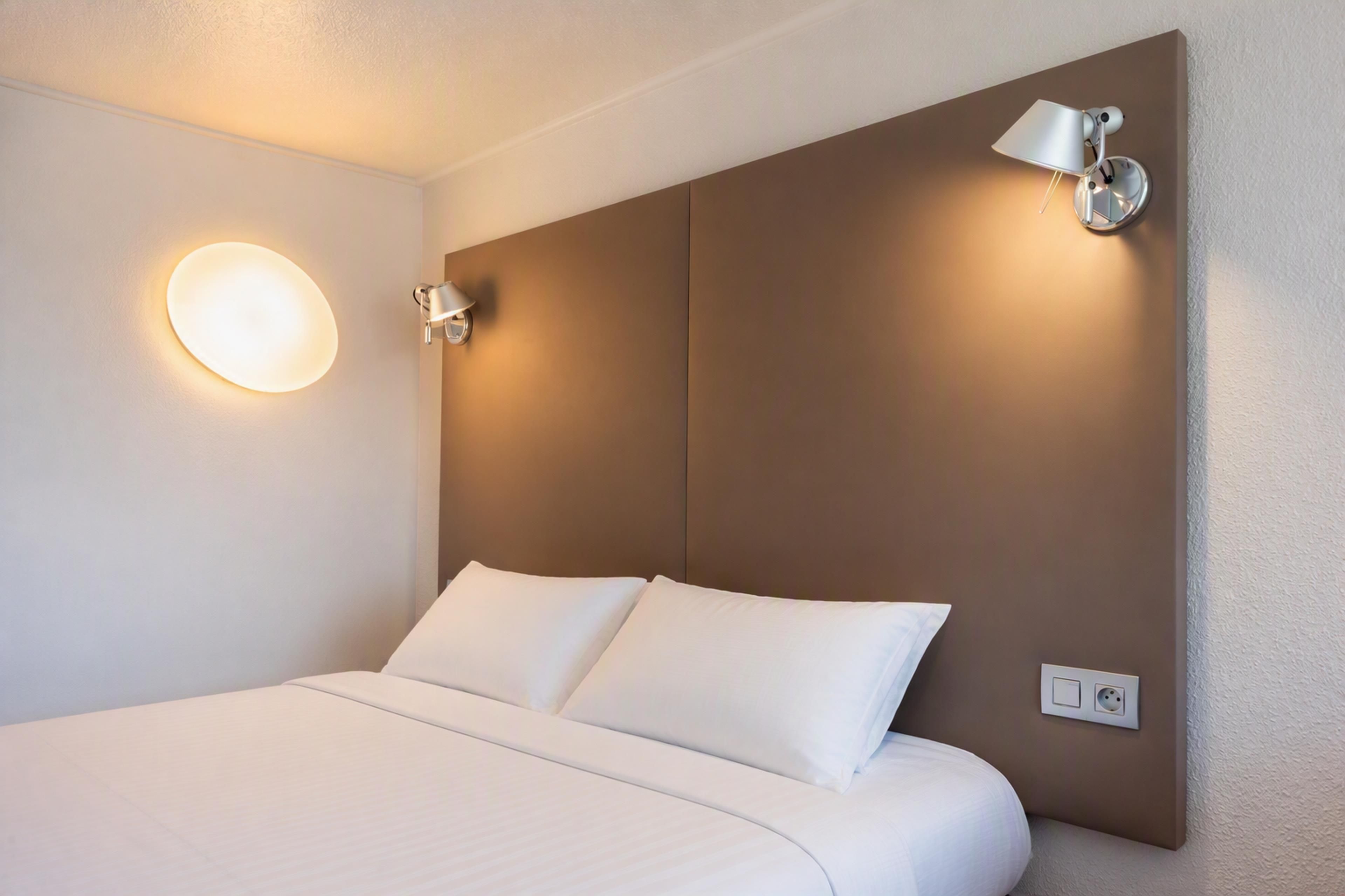 Una camera d'albergo con un letto grande, due lampade a parete e una presa elettrica.