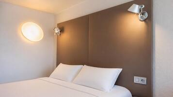 Una camera d'albergo con un letto grande, due lampade a parete e una presa elettrica.