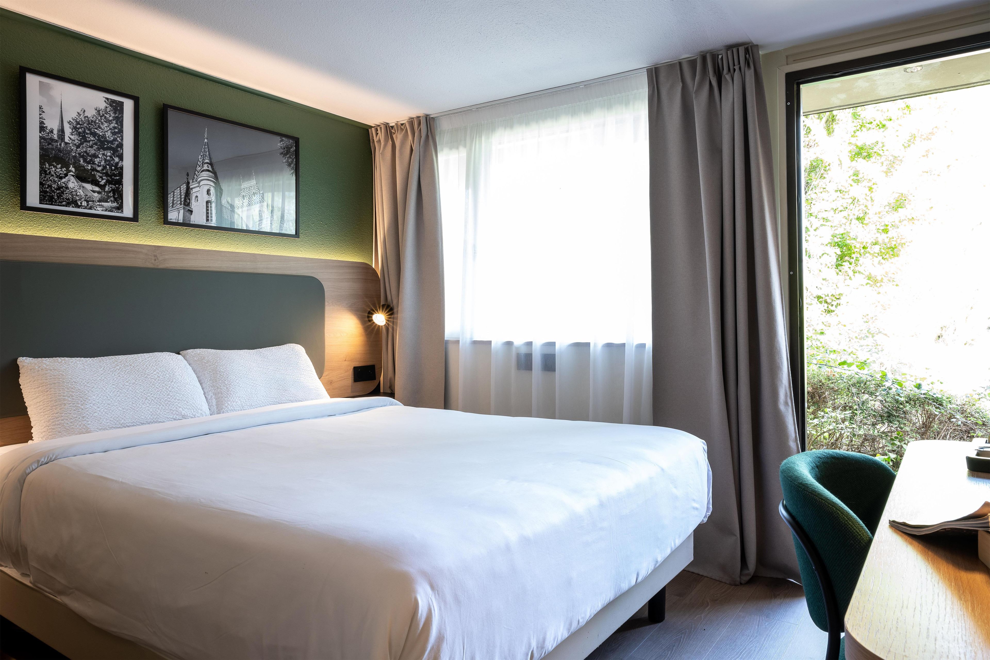 Ein Hotelzimmer mit Bett, Schreibtisch und einem Fenster mit Vorhängen.