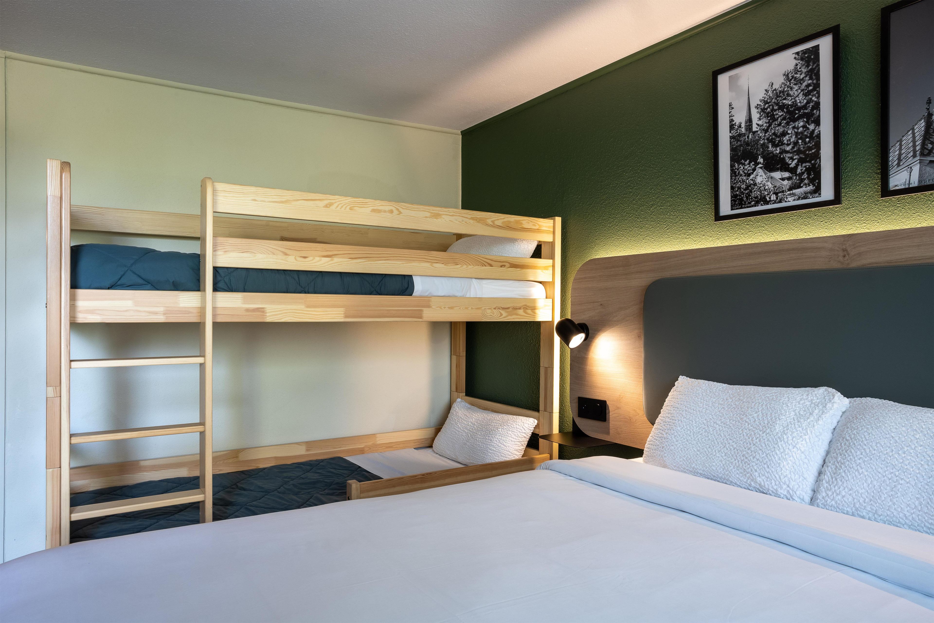 A bunk bed room with a ladder, a bedside table with a lamp, and two framed pictures on the wall.