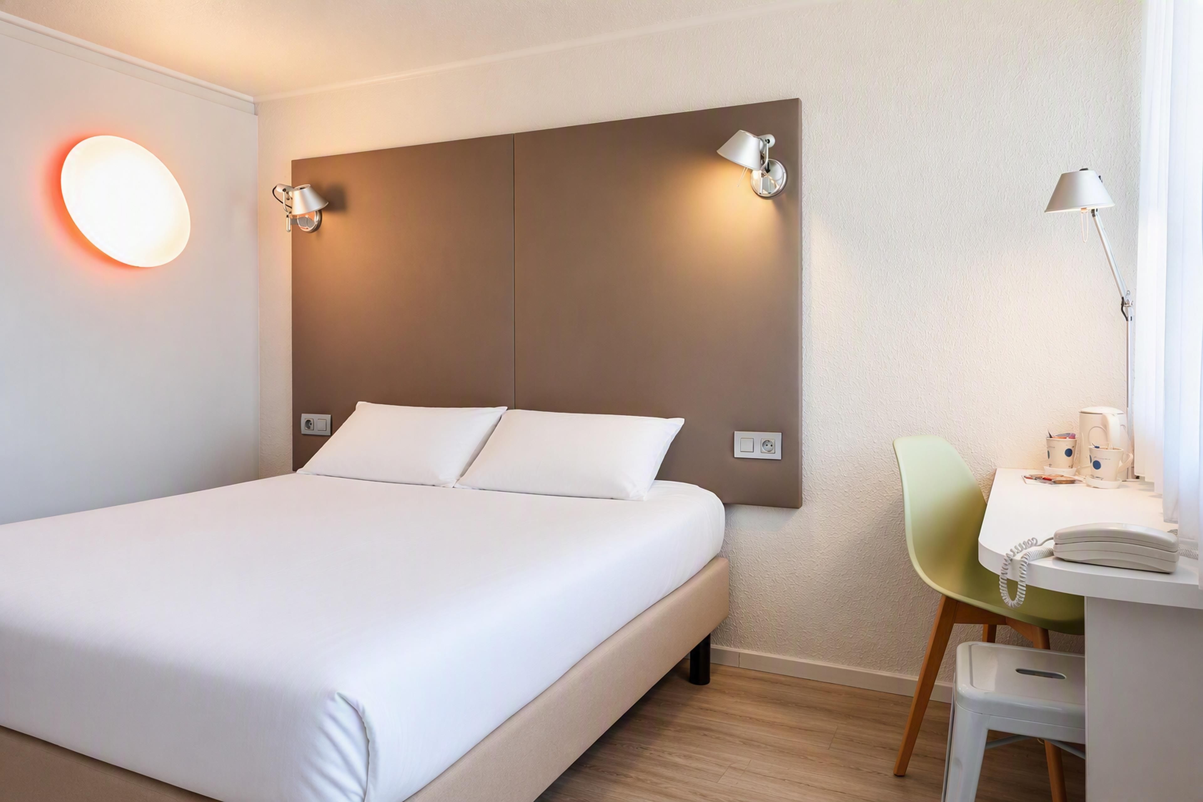 A hotel room with a bed, bedside lamps, a desk with a telephone, and a chair.