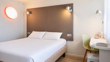 A hotel room with a bed, bedside lamps, a desk with a telephone, and a chair.
