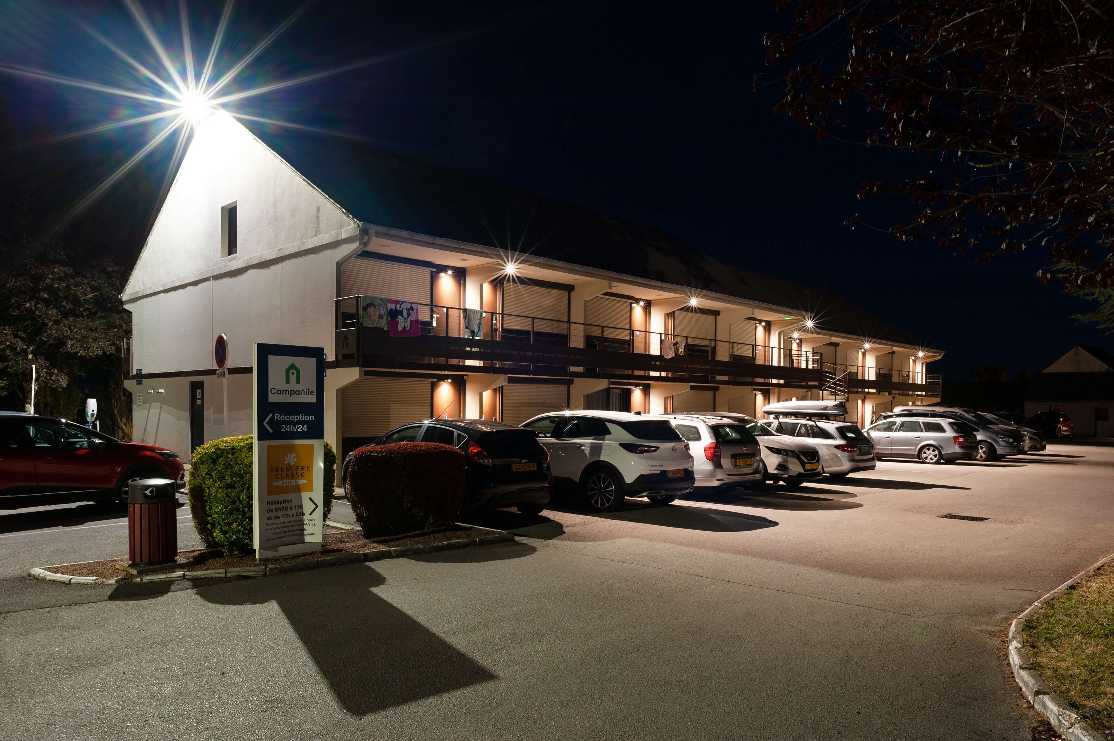 Hotel med reception, flere parkeringspladser og oplyst facade om natten.