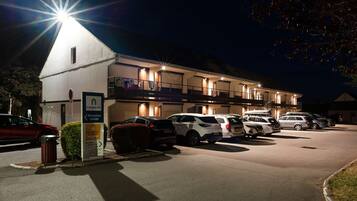Hotel med reception, flere parkeringspladser og oplyst facade om natten.