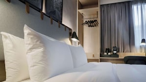 A neatly made bed with white linens, a bedside table with a lamp, and a wooden headboard.