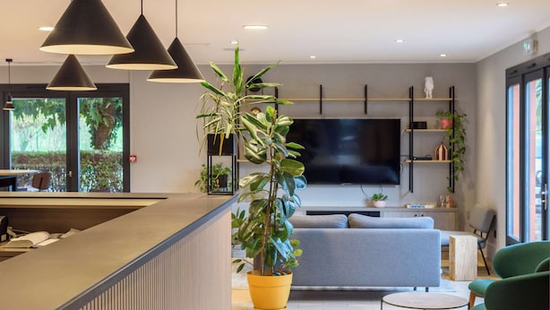 A modern living room with a sofa, a coffee table, and a TV mounted on the wall. There are potted plants and a staircase leading to an upper level.
