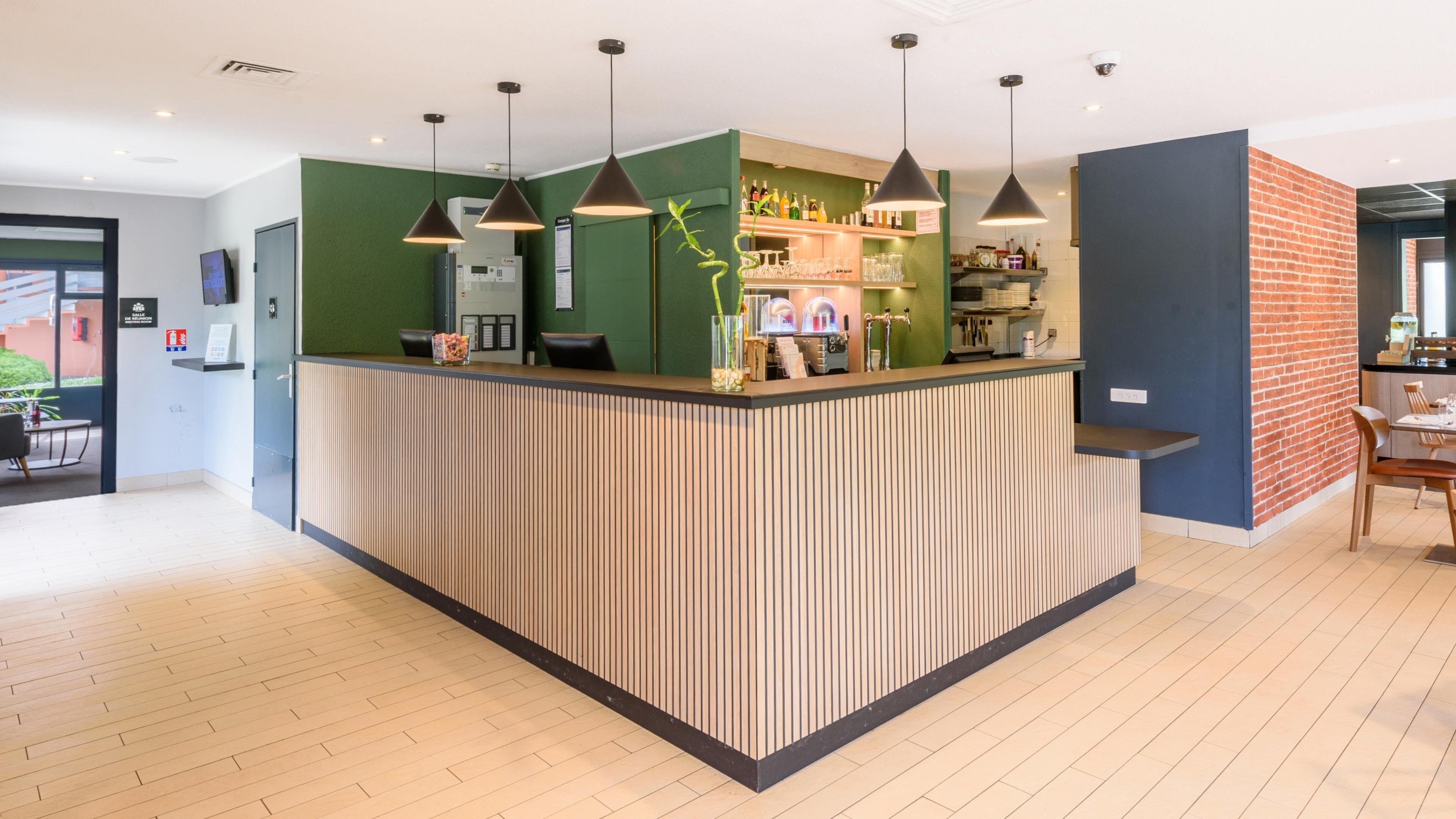 Un espace d’accueil moderne avec un comptoir de réception en bois, des murs verts et des luminaires suspendus.