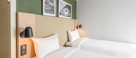 Habitación de hotel con dos camas, una pared verde y dos cuadros enmarcados.