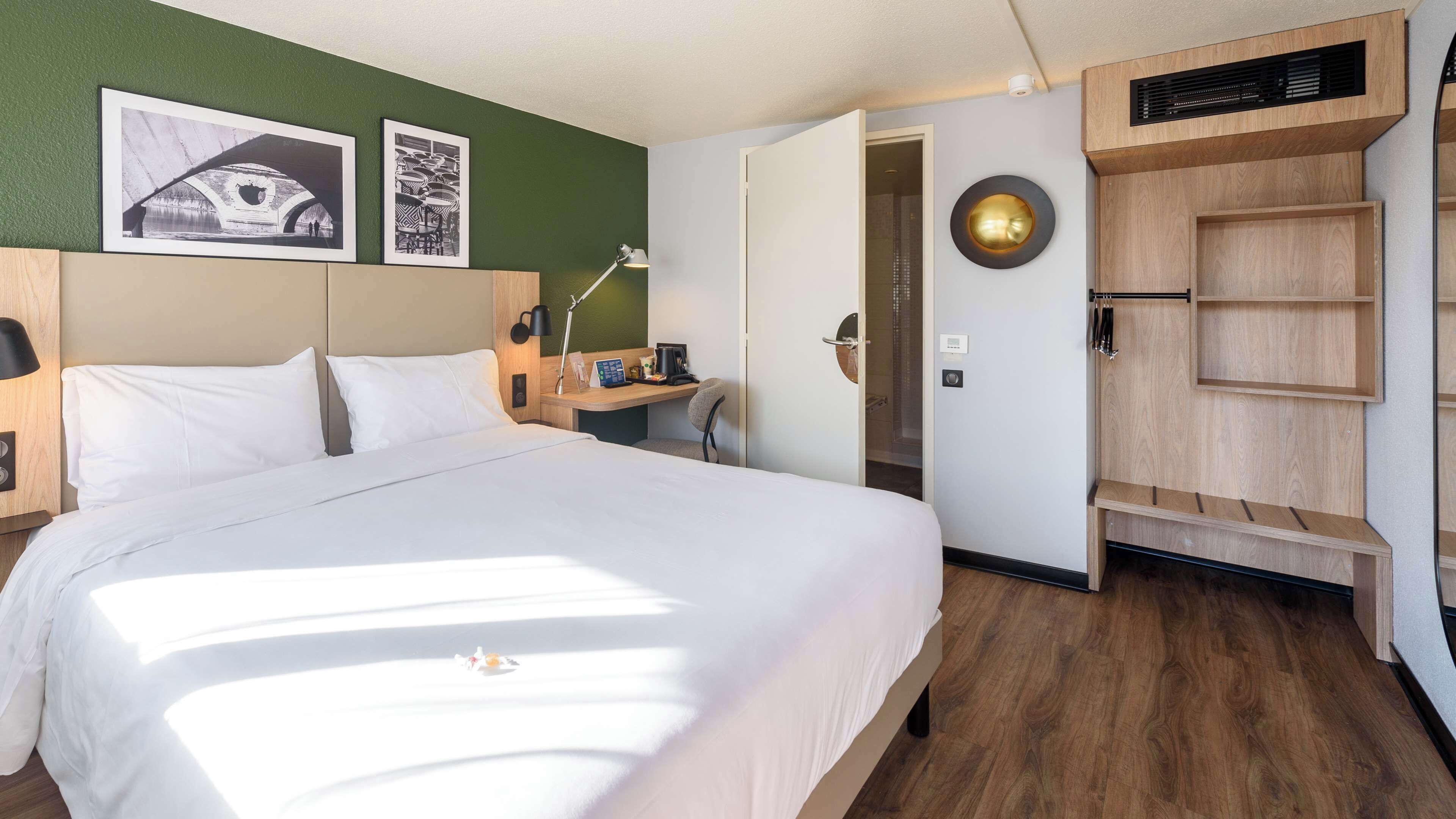 A hotel room with a large bed, a desk, a chair, and a wardrobe.