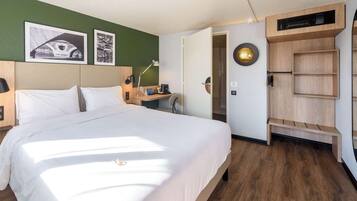 A hotel room with a large bed, a desk, a chair, and a wardrobe.