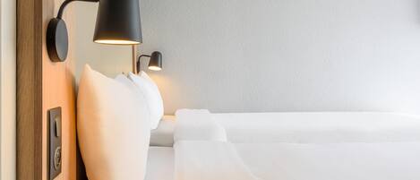 A neatly made bed with white linens, a wall-mounted lamp, and a wooden panel on the left.