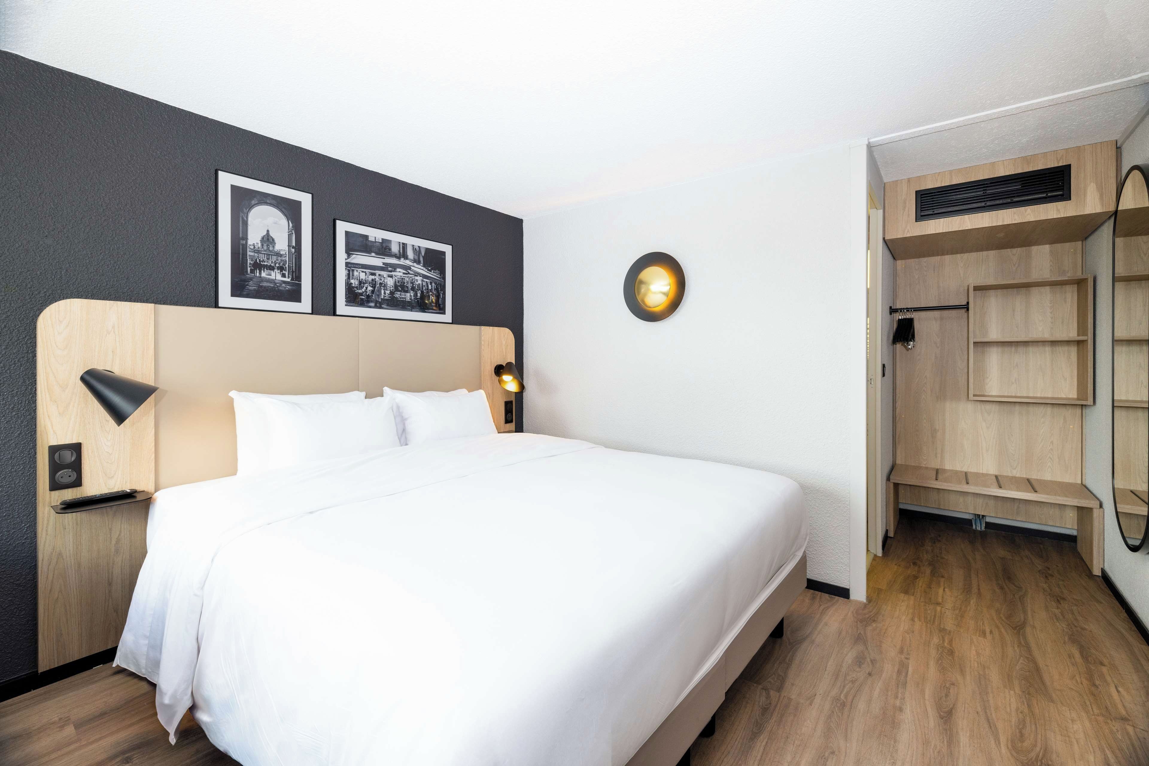 Un lit bien fait, avec du linge de lit blanc, une tête de lit en bois et deux lampes fixées au mur.