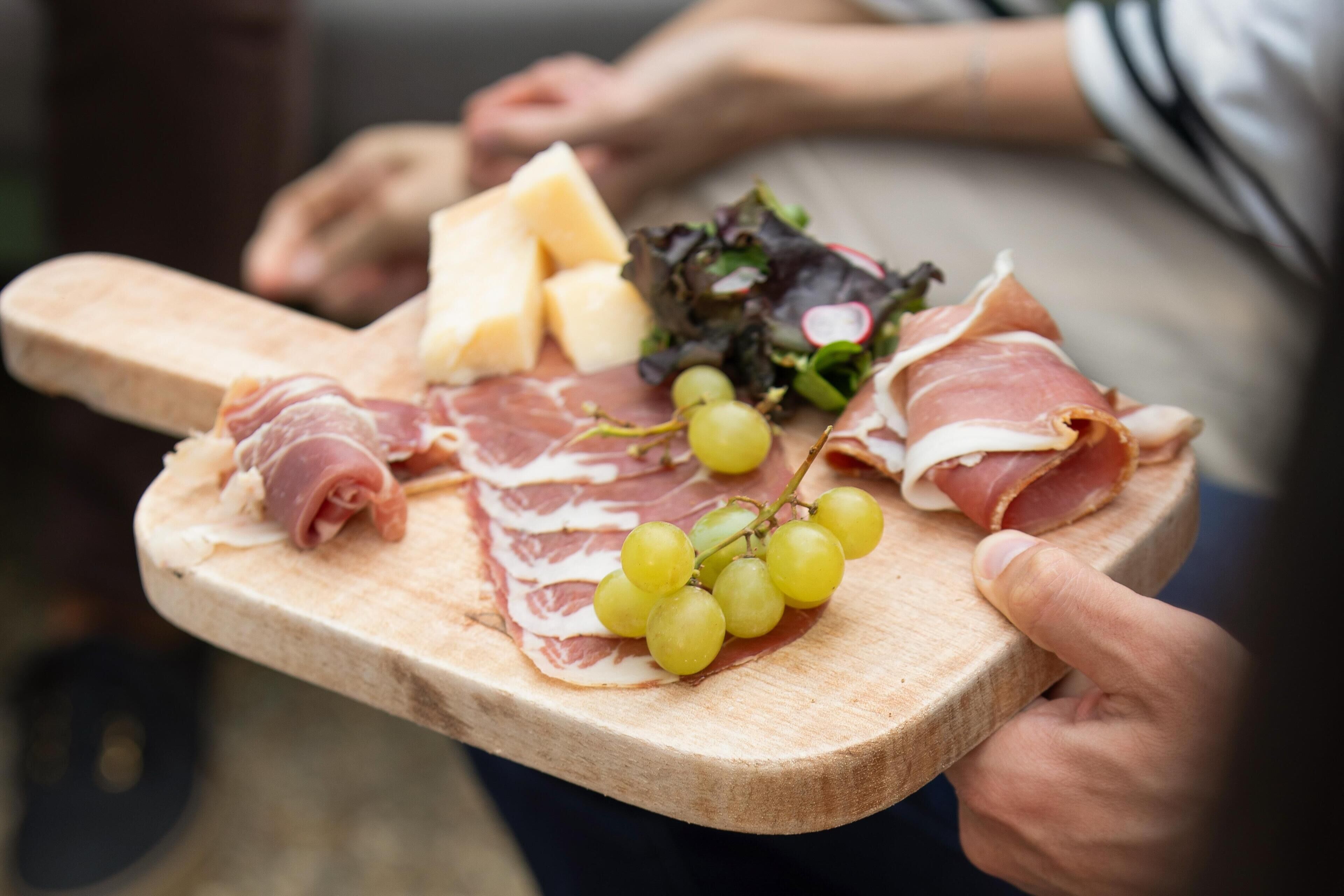 A wooden board with various cheeses, cured meats, and grapes.