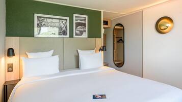 Camera d'albergo con un letto, due cuscini, un comodino con una lampada, uno specchio e due quadri appesi al muro.