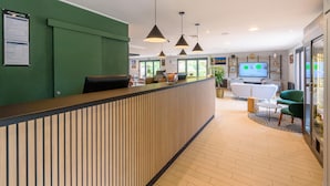 A reception area with a wooden reception desk, green walls, pendant lighting, a seating area with a sofa and chairs, and a television screen displaying a menu.