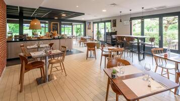 A restaurant with a modern interior, wooden furniture, and large windows offering a view of the outdoors.