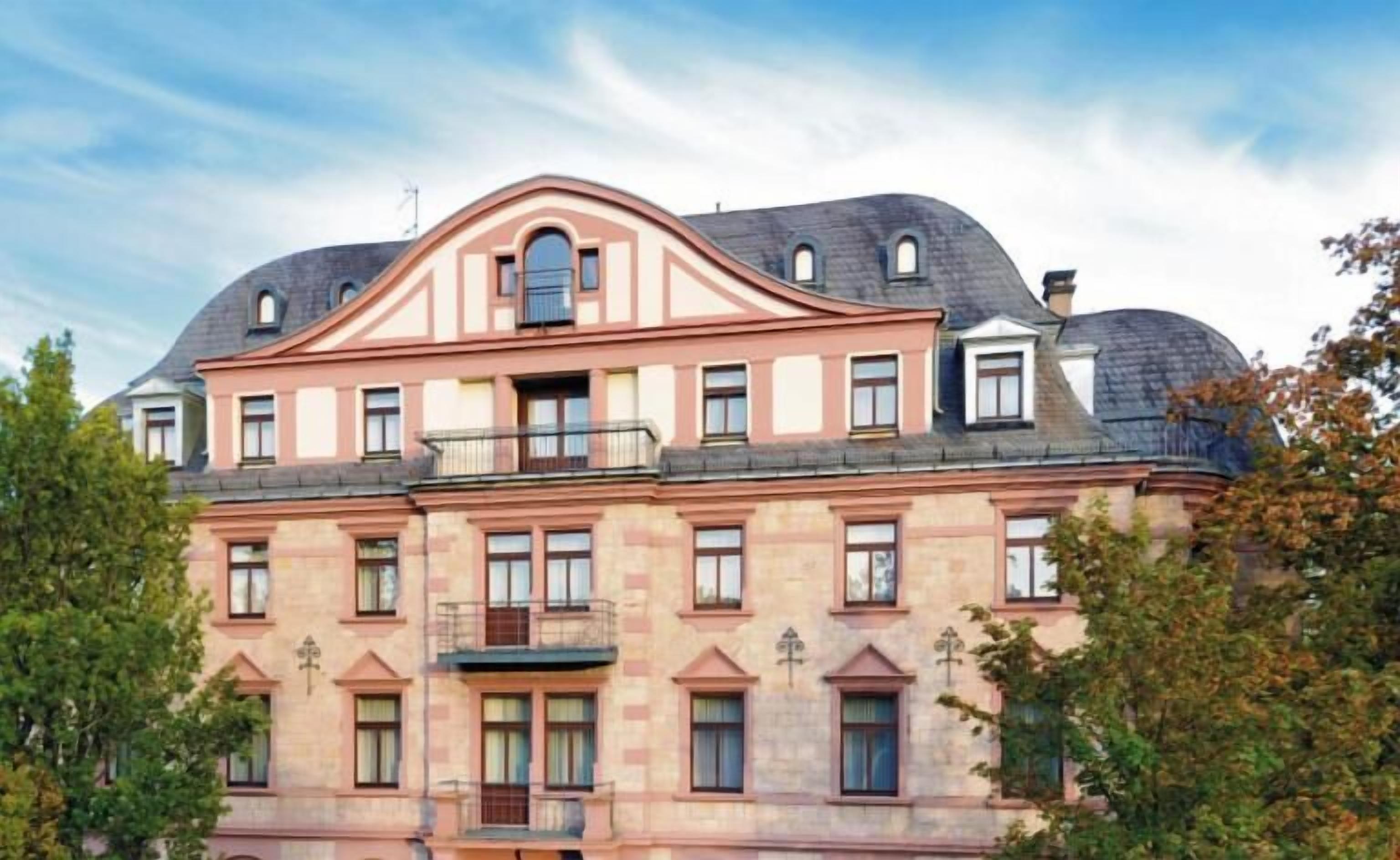 Un edificio de varios pisos con fachada simétrica, ventanas amplias y un balcón central.
