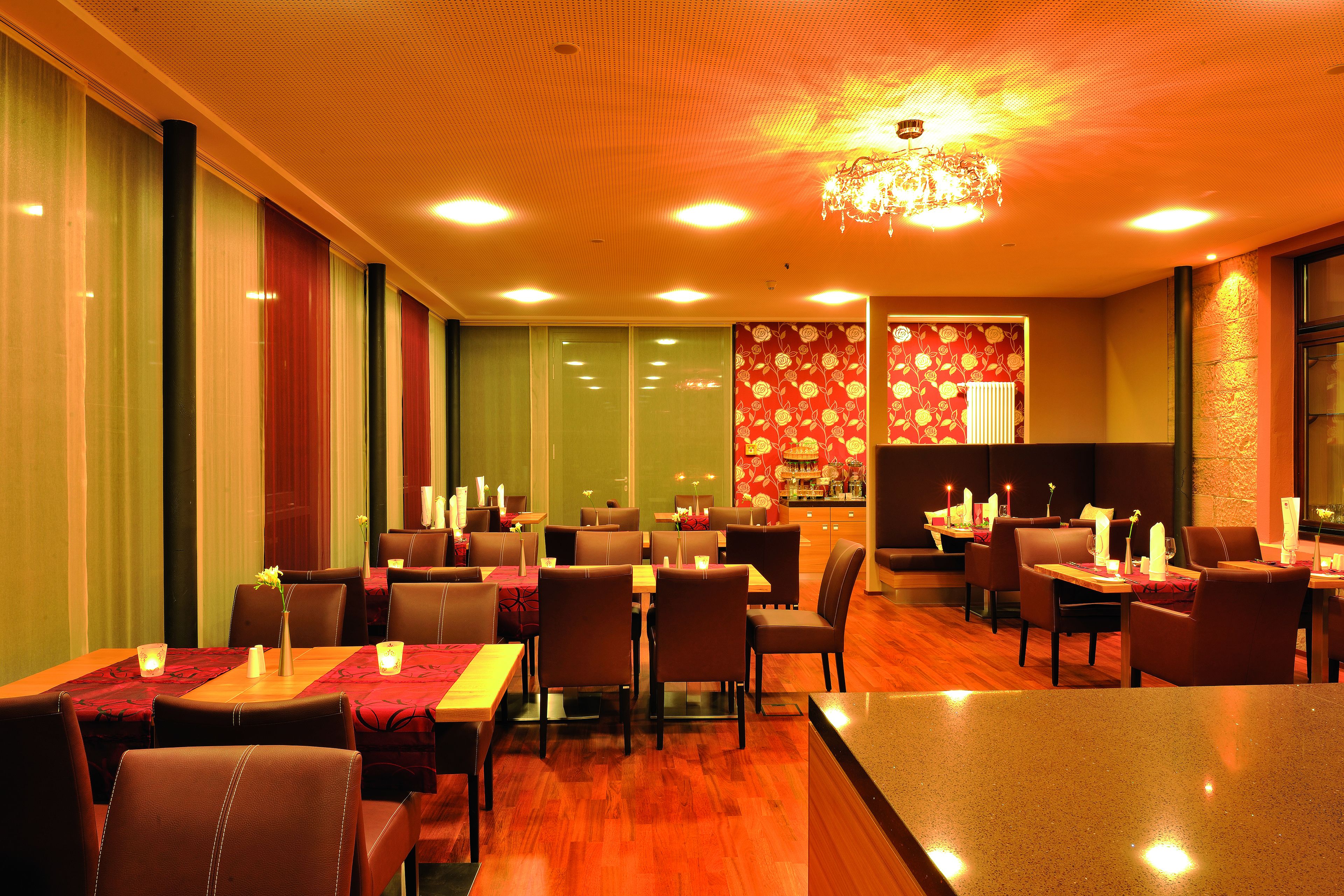 Un restaurante con varias mesas y sillas, velas en cada mesa y una pared con un diseño decorativo al fondo.