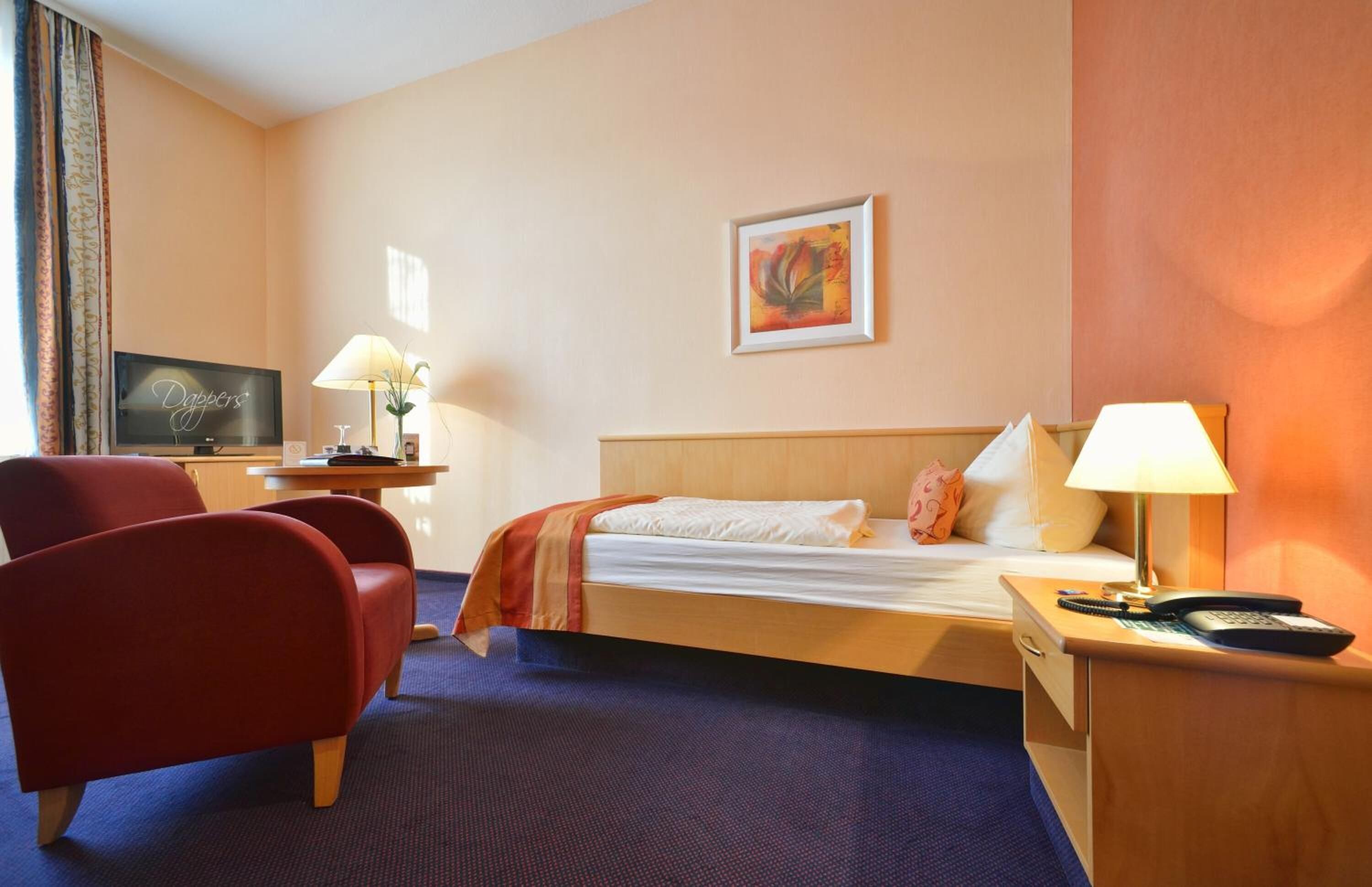 Una habitación de hotel con cama, escritorio, silla, televisor y un cuadro en la pared.