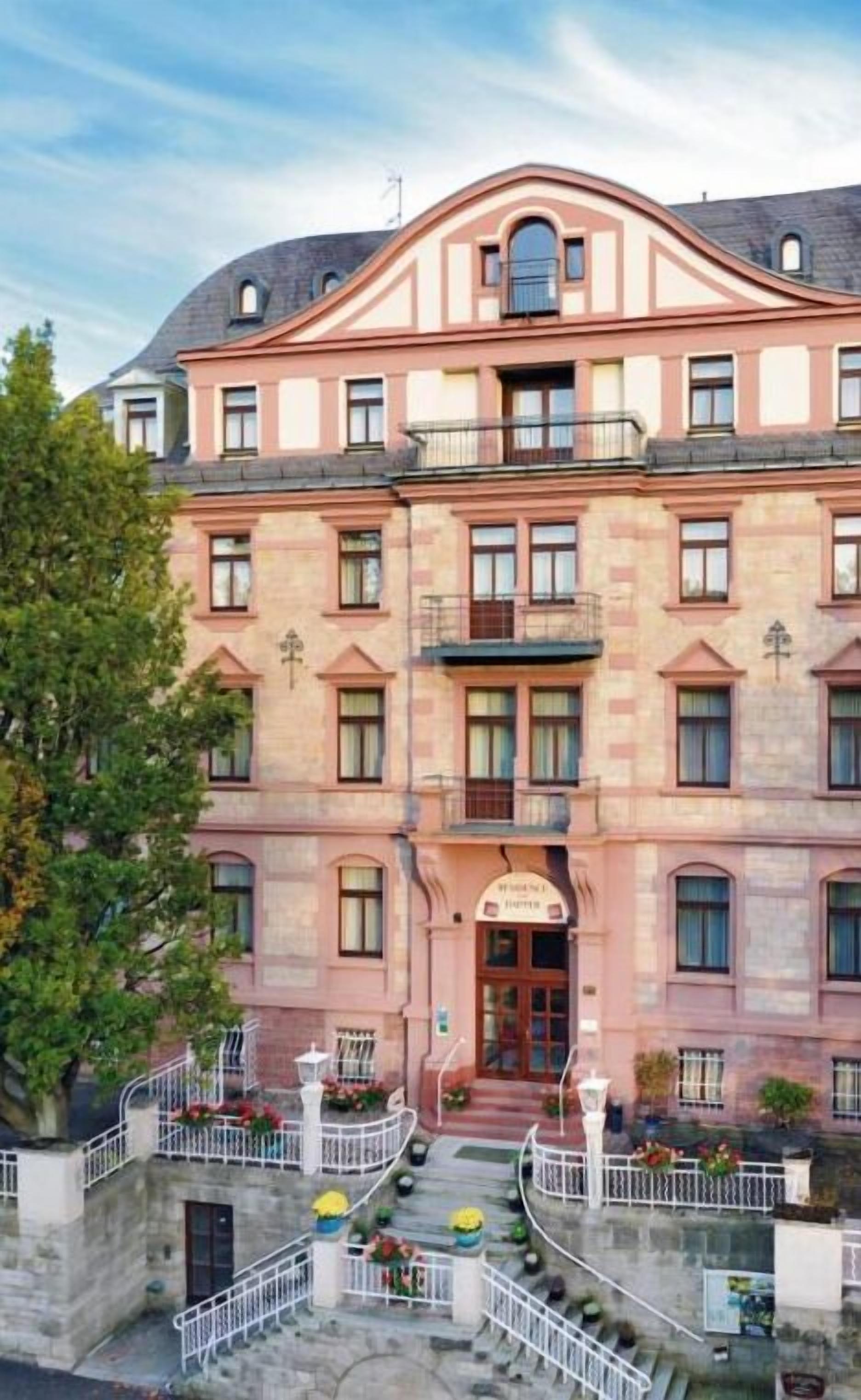 Un edificio de varios pisos con una entrada central, balcones y un patio con escaleras.