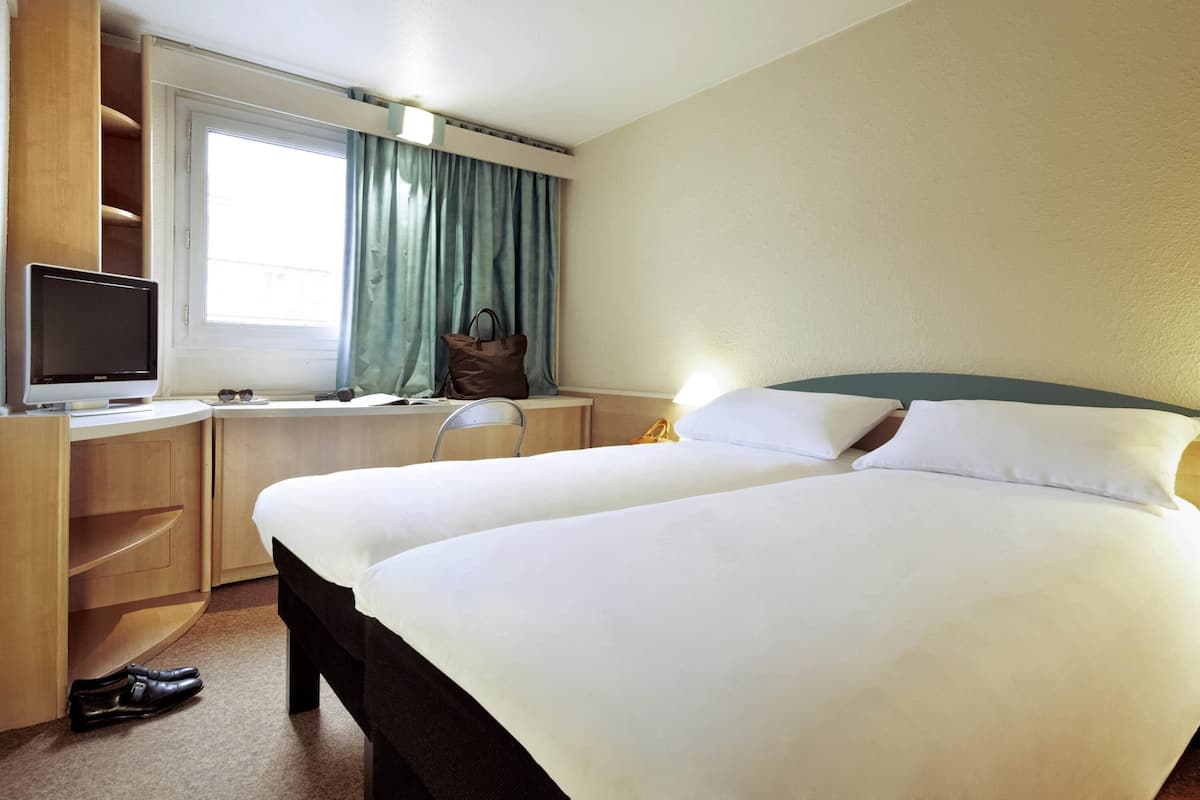 A hotel room with a bed, a desk, a television, a window with curtains, and a chair.