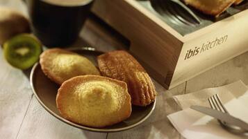 Une boîte en bois portant l’inscription « Cuisine Ibis », avec des pâtisseries sur une assiette et une tasse de café.