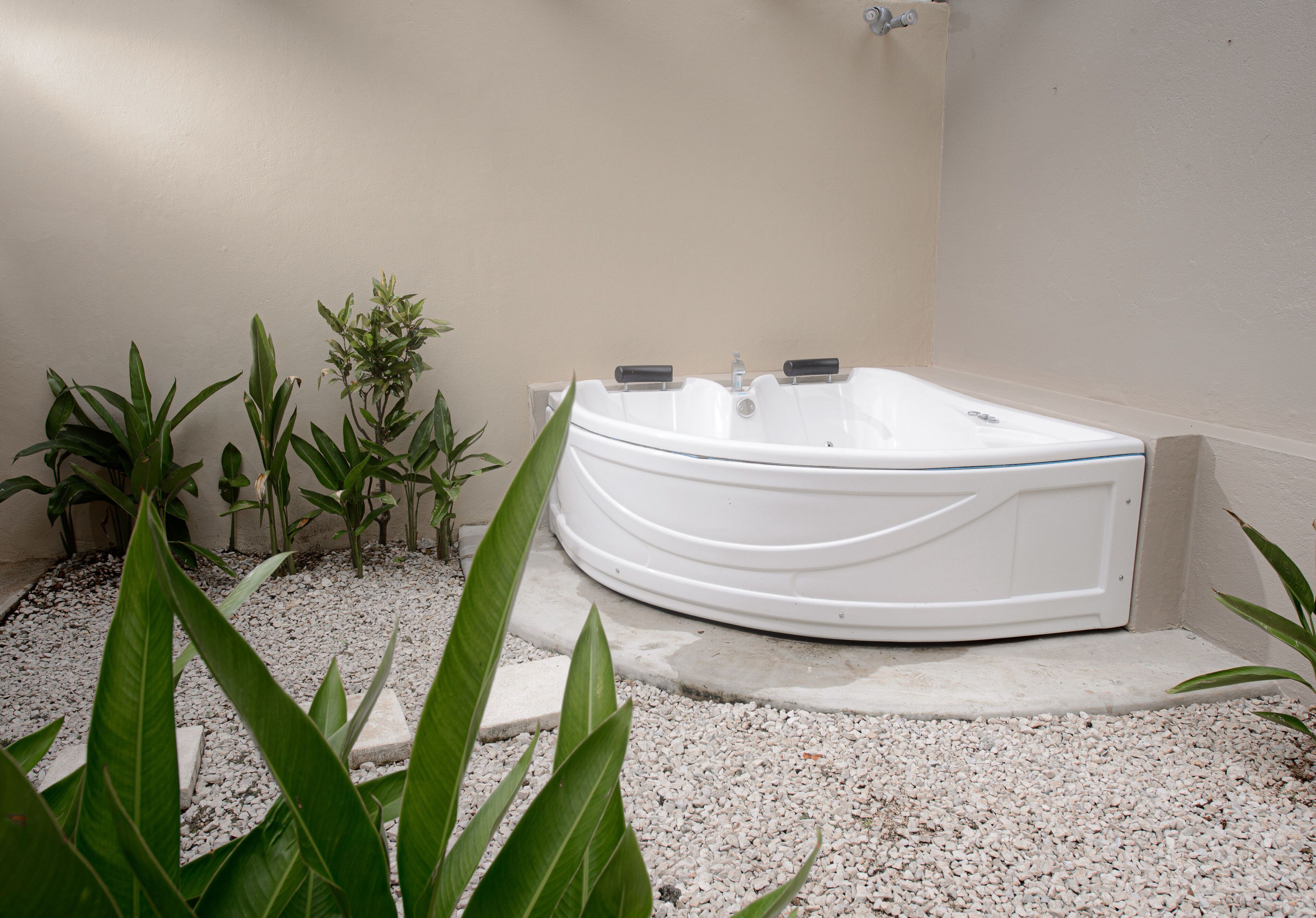 Zona de spa con un jacuzzi blanco rodeado de grava y plantas en macetas.