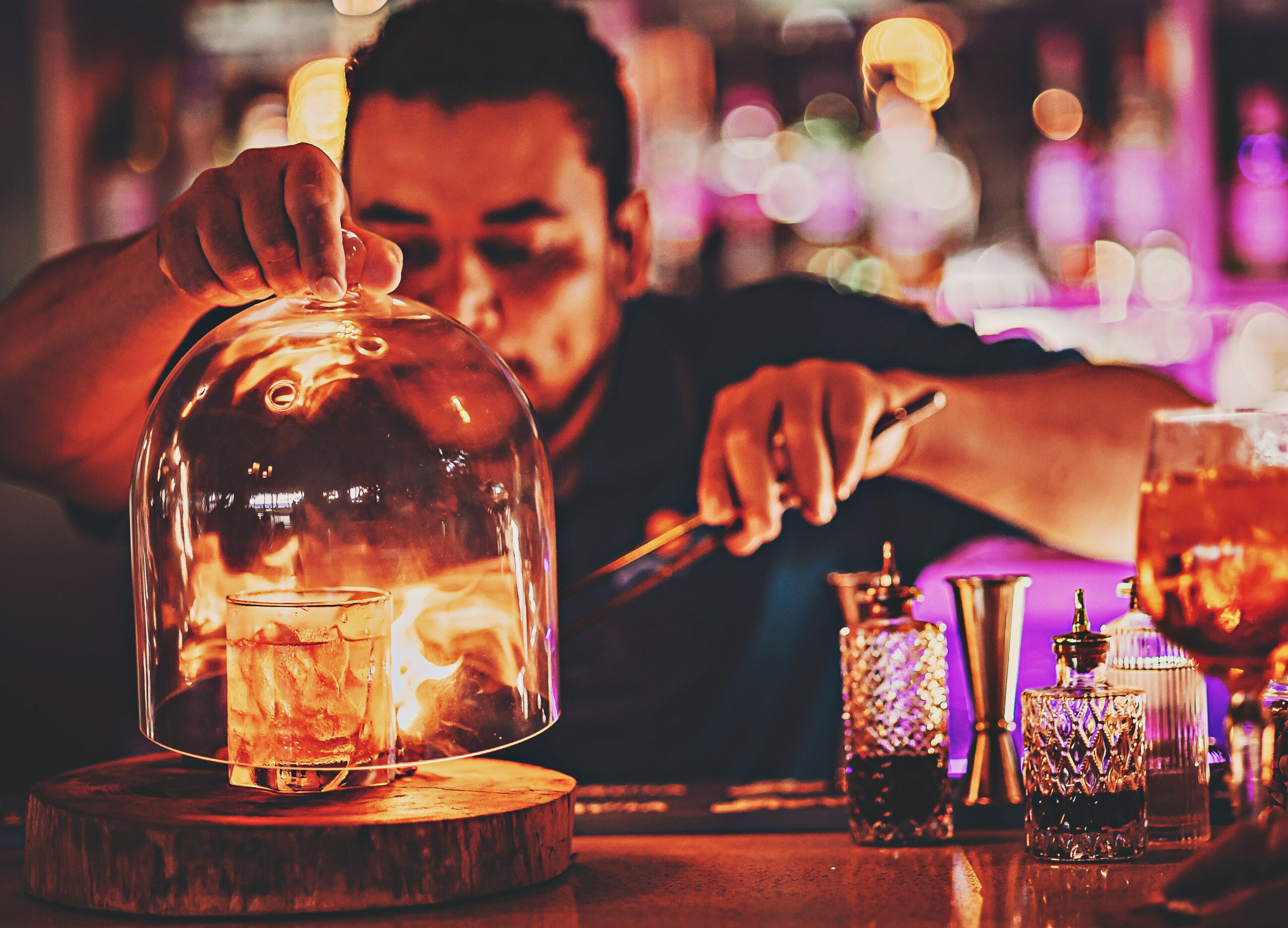 Ein Barkeeper bereitet einen Cocktail hinter einer Glaskuppel zu.